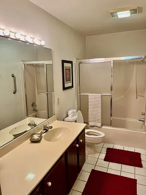 Bathroom with a sink, toilet, tub, and red rugs on the floor.