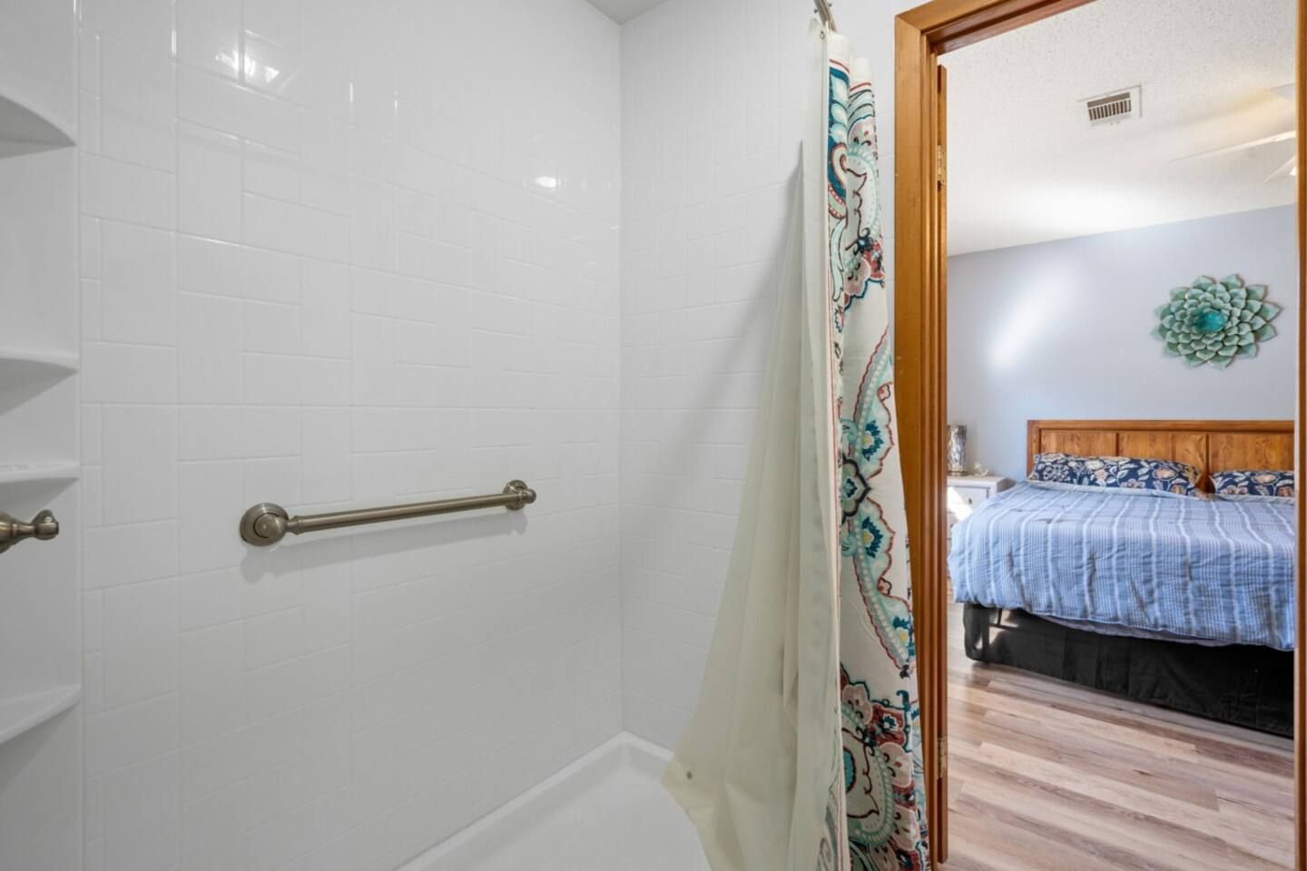 A bathroom with a shower and a bed in the background.