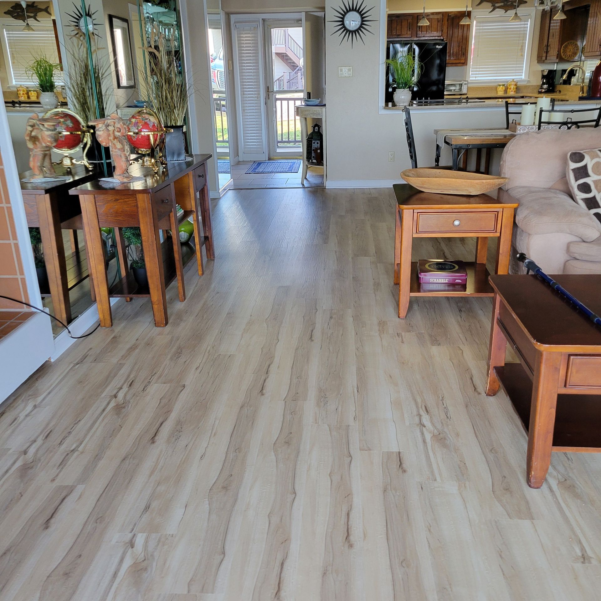 Living room with wood flooring, wood furniture, and a view of a deck through an open door.