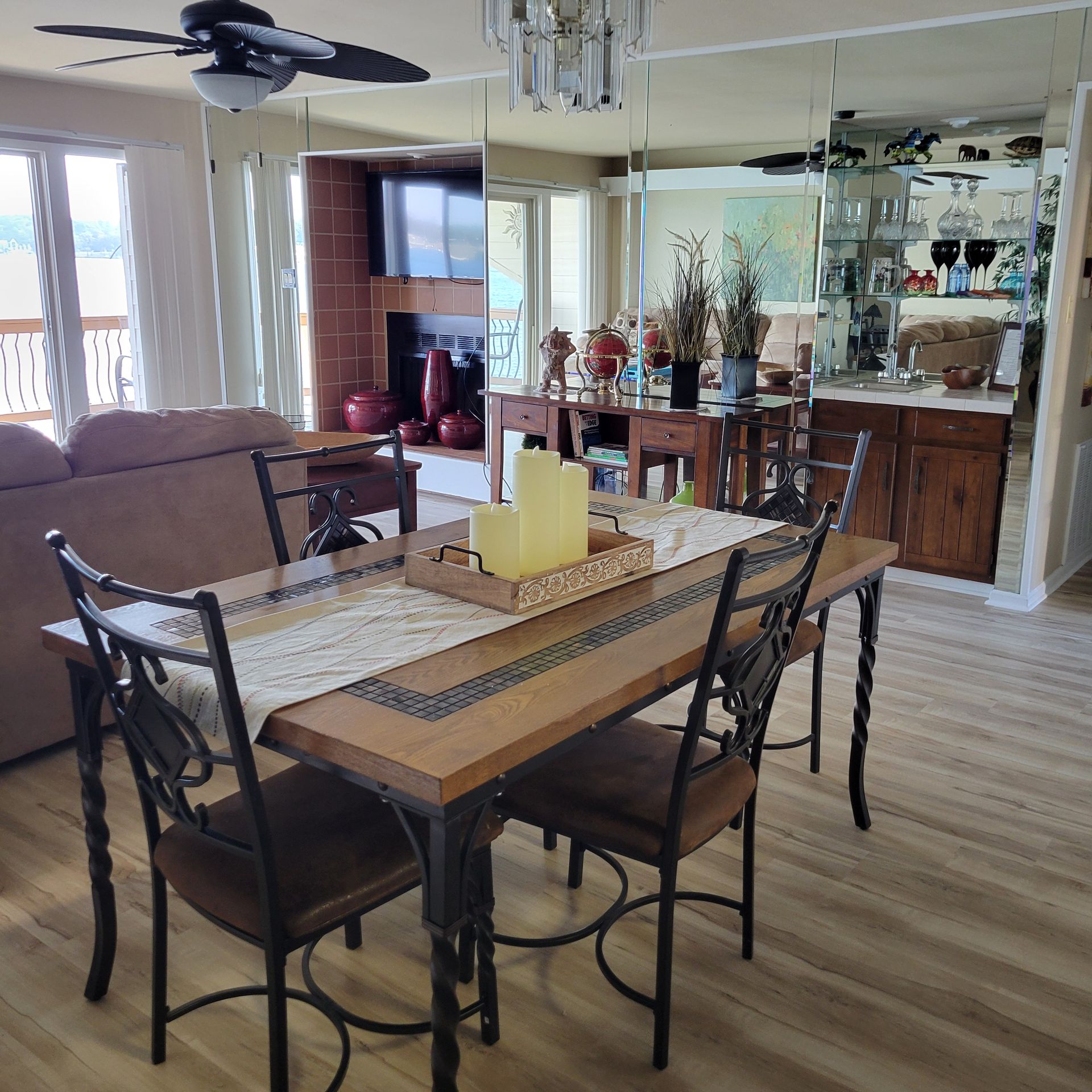 Dining room with wooden table and chairs, tan sofa, fireplace, and mirrored wall.