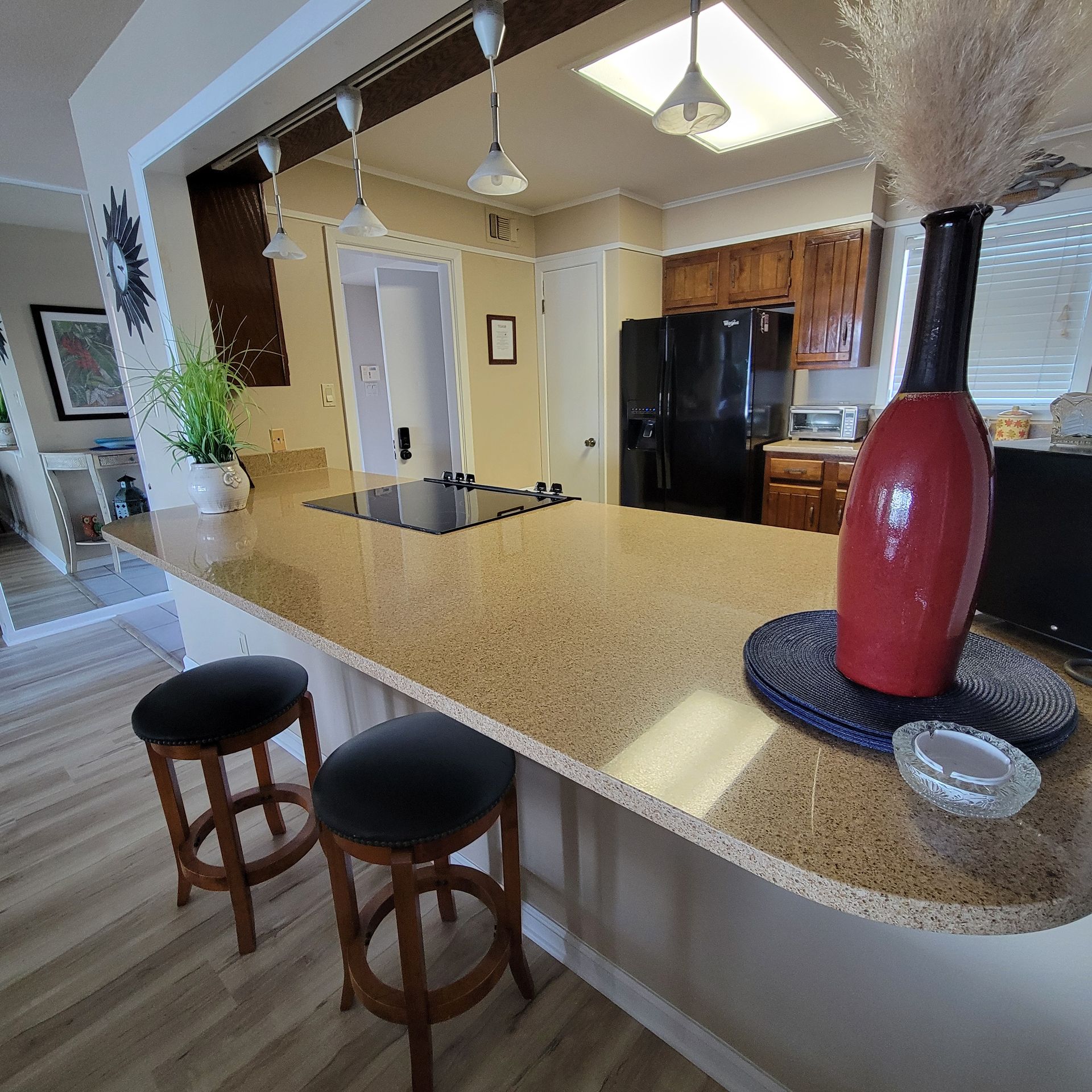 Kitchen with countertop and stools, black appliances, brown cabinets, and a tall vase.