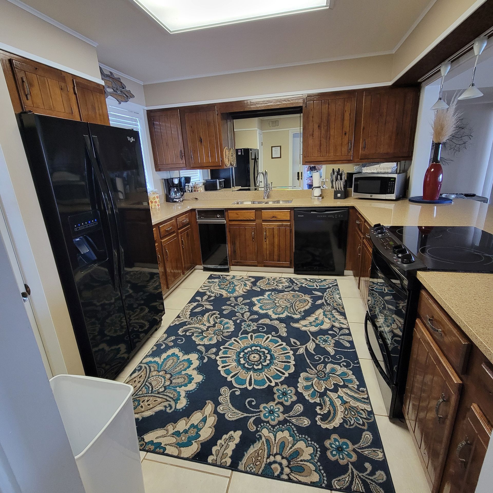 Kitchen with wood cabinets, black appliances, a blue patterned rug, and a rectangular window.