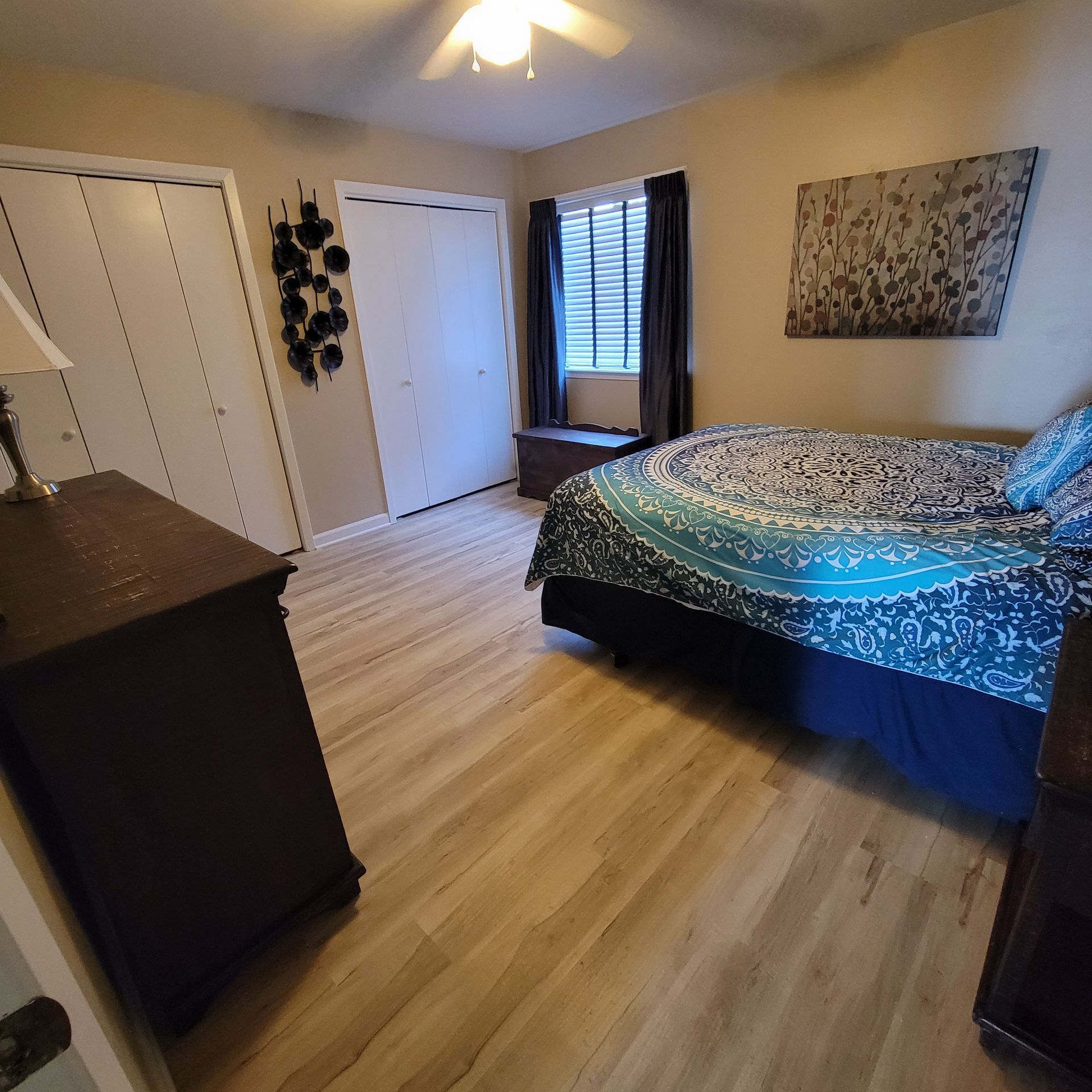 Bedroom with bed, dresser, closet, window, and wall art. Light brown floors.