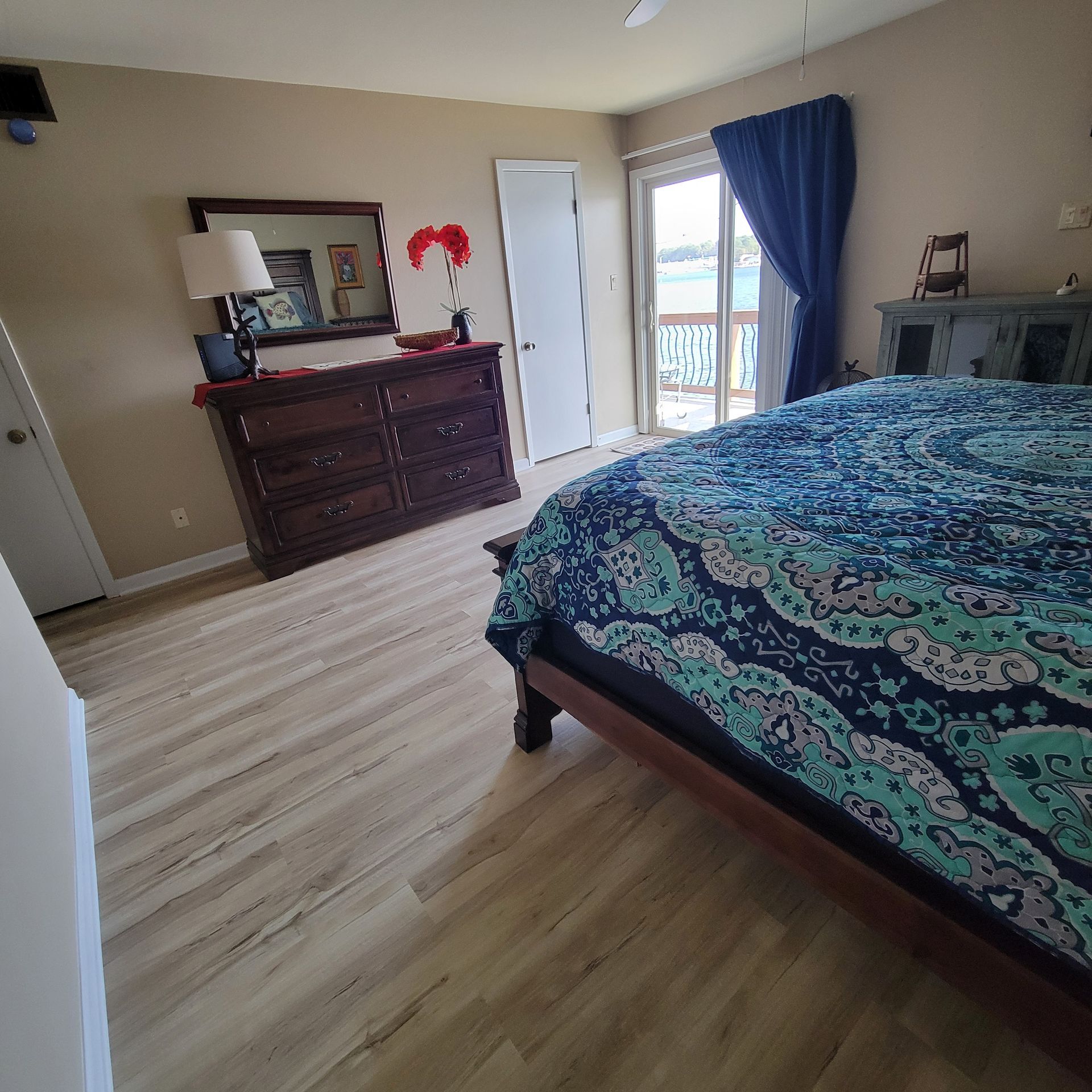 Bedroom with bed, dresser, door to balcony, and hardwood-style flooring.