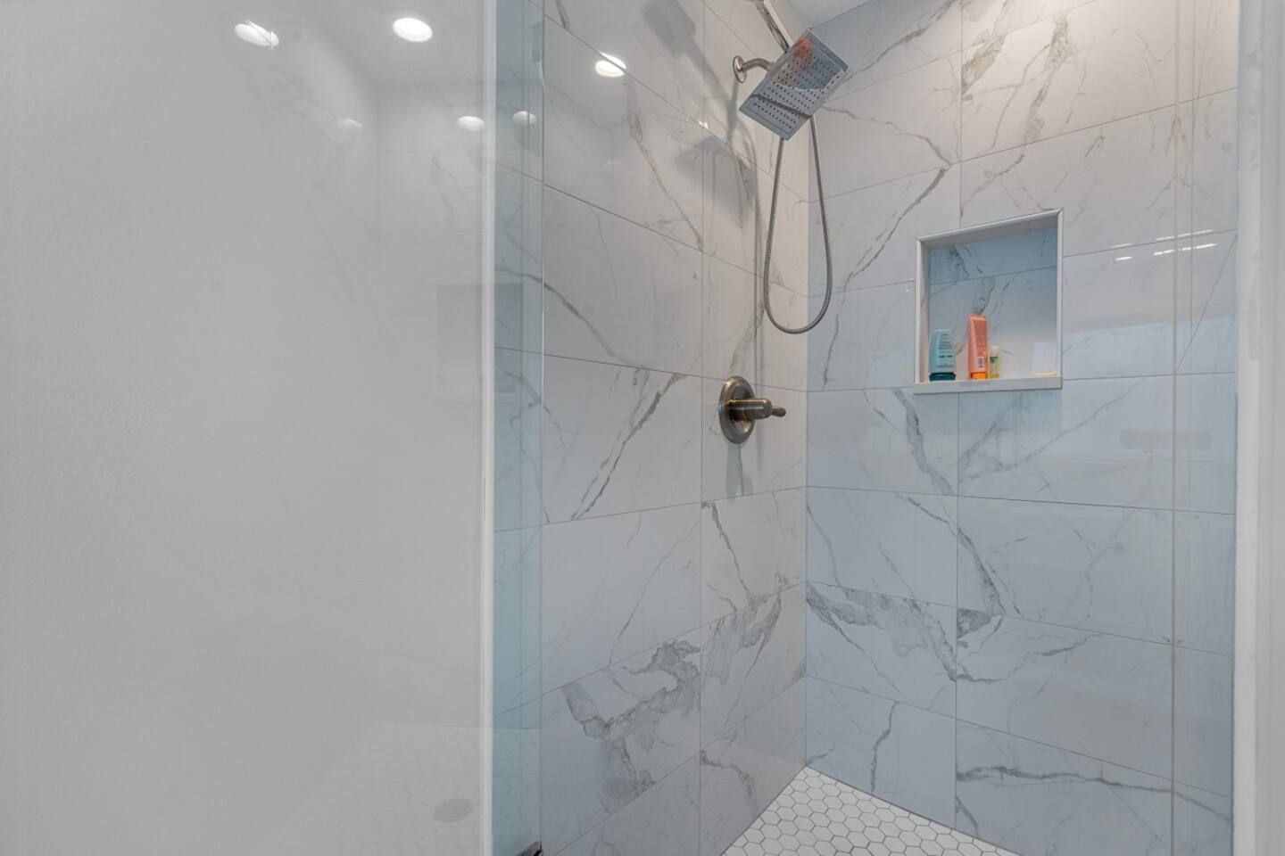A bathroom with marble tiles and a walk in shower with a glass door.