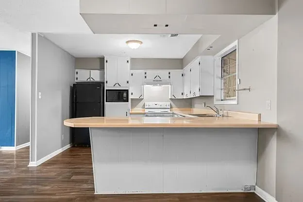 An empty kitchen with white cabinets and a black refrigerator.