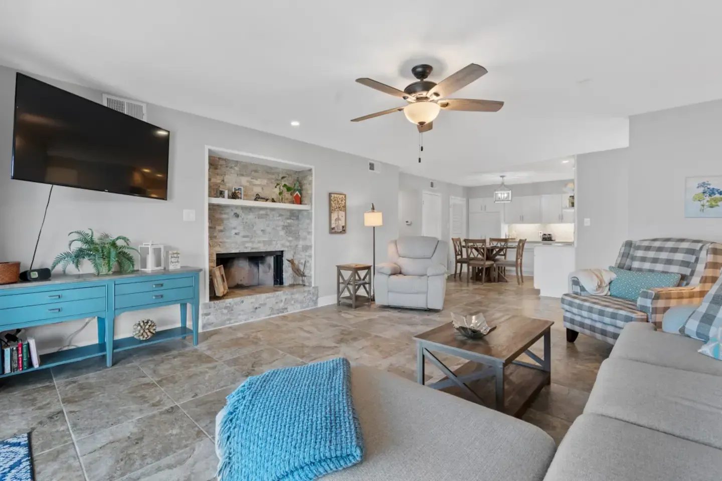A living room with a couch , chairs , a television and a ceiling fan.