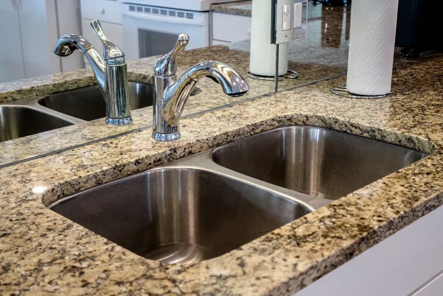 A kitchen sink with two sinks and a faucet on a granite counter top.