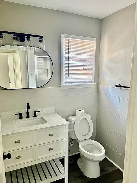 A bathroom with a toilet , sink , mirror and window.