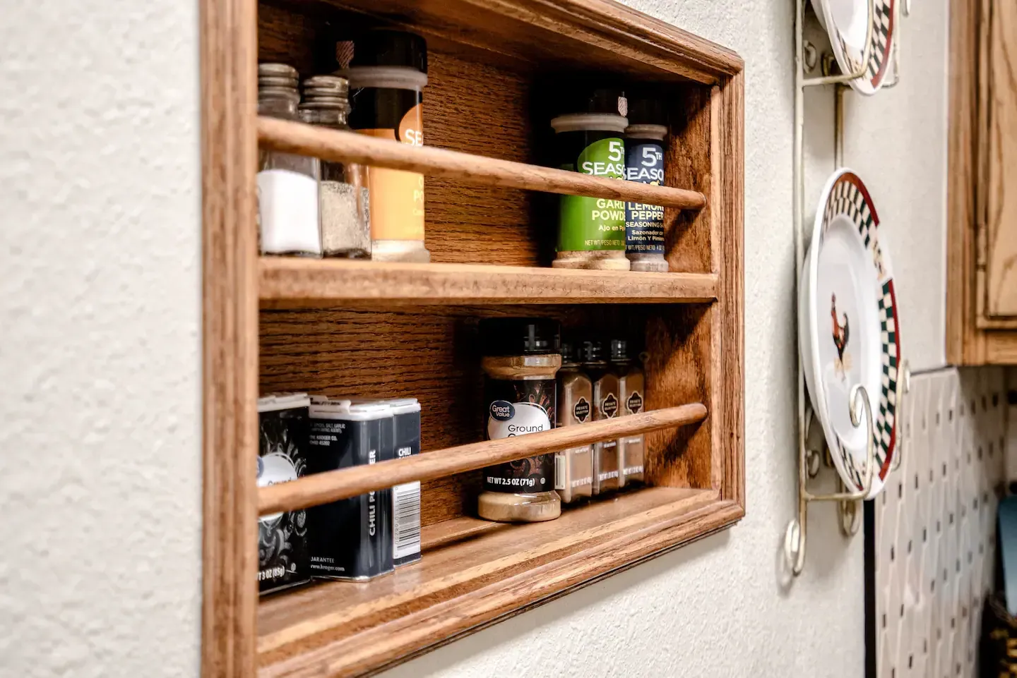 A wooden spice rack is built into a wall in a kitchen.