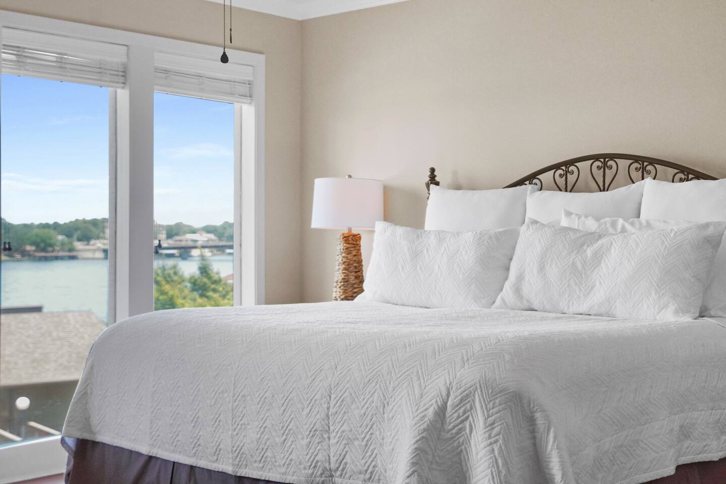 A bed with white sheets and pillows in a bedroom with a view of a lake.