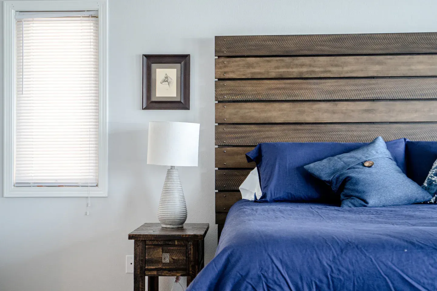 A bedroom with a bed , nightstand , lamp and wooden headboard.