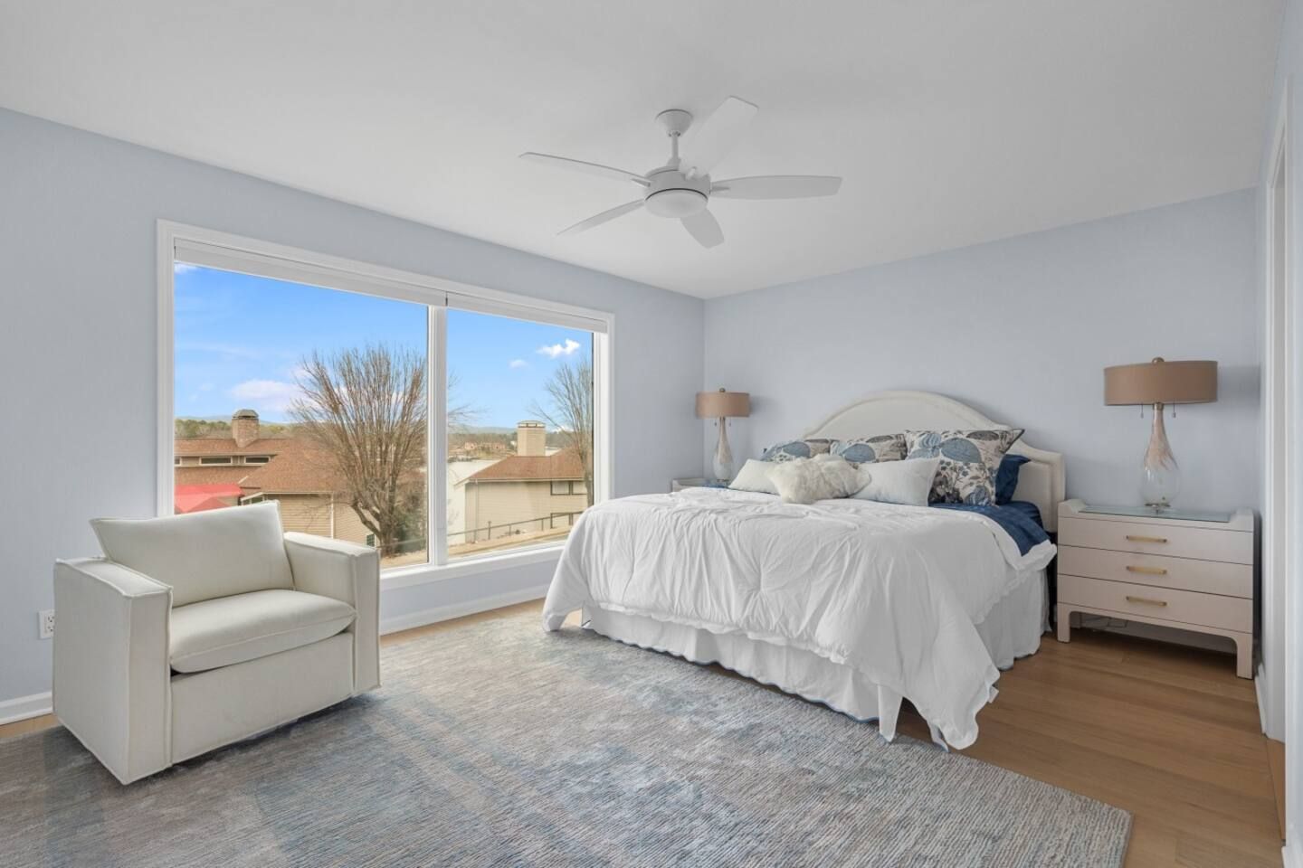 A bedroom with a large bed , chair , nightstand and ceiling fan.