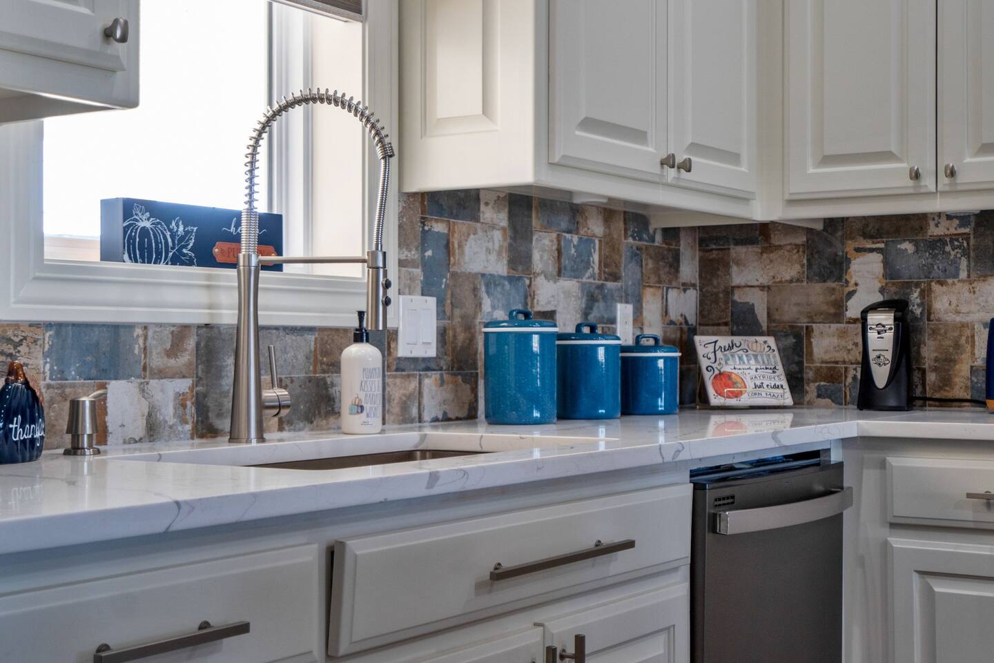 A kitchen with white cabinets , a sink , a dishwasher , and a window.