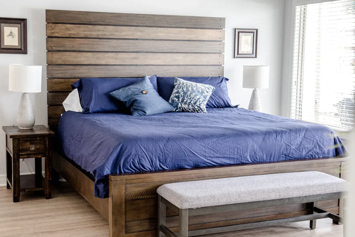 A bedroom with a bed , nightstand , bench and lamps.