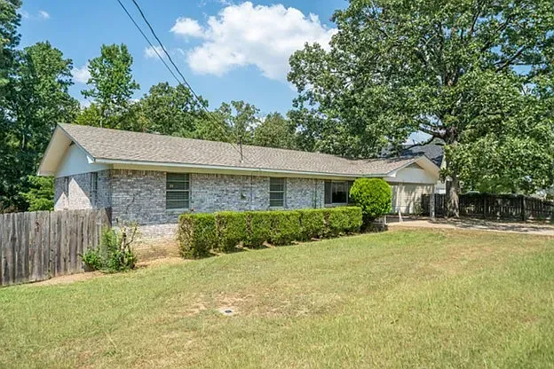 A brick house with a fence and a large lawn in front of it.