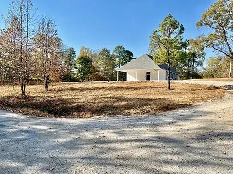 A white house is sitting in the middle of a dirt field surrounded by trees.