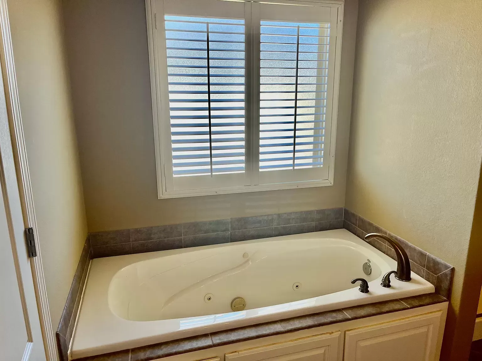 A bathtub in a bathroom next to a window with shutters.