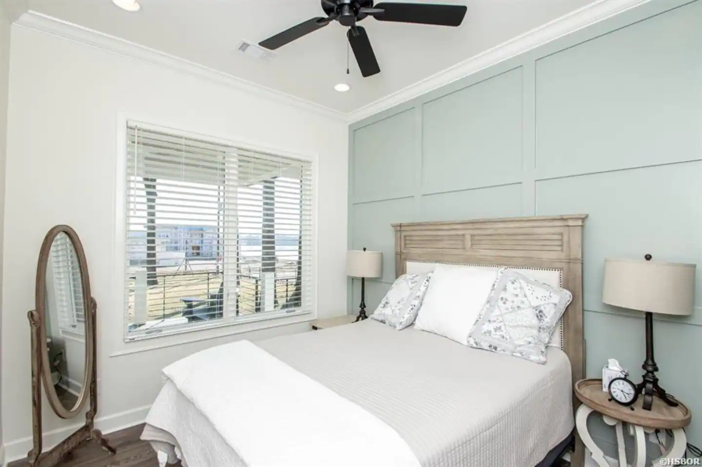 A bedroom with a bed , mirror , lamp and ceiling fan.
