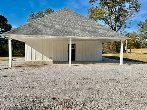 A white house with a gray roof is sitting on top of a gravel lot.