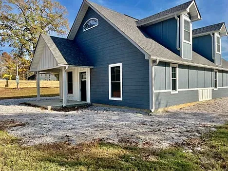 A blue house with a gray roof is sitting in the middle of a grassy field.