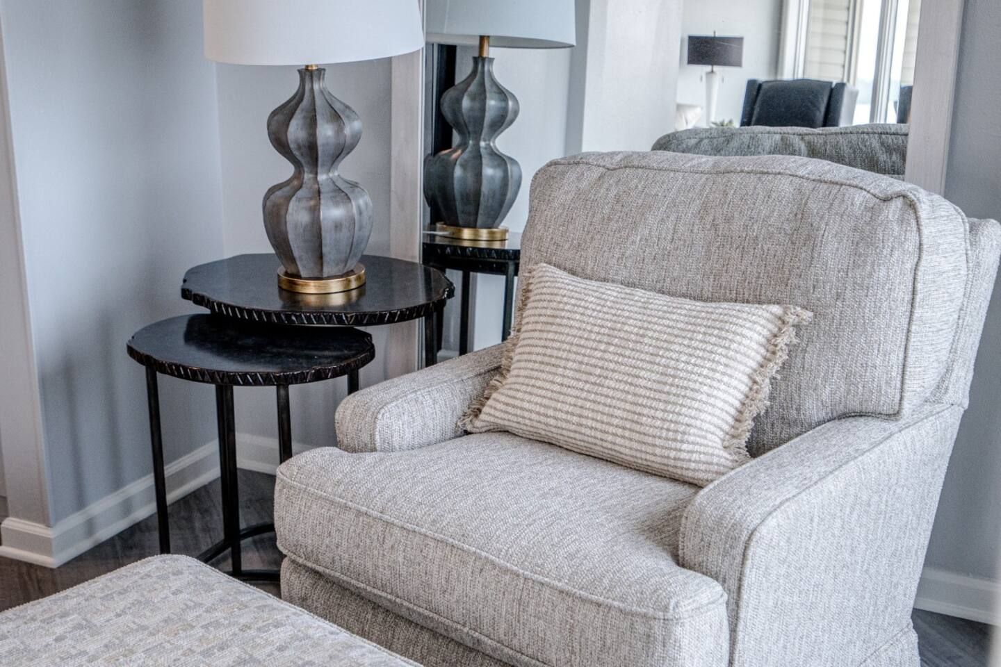 A living room with a chair , ottoman , lamps and a mirror.