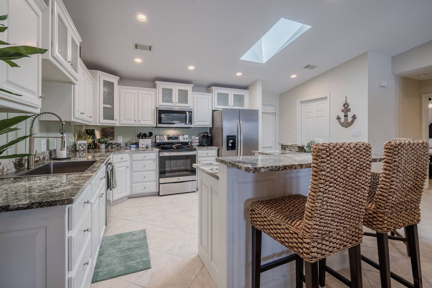 A kitchen with white cabinets , granite counter tops , stainless steel appliances and wicker bar stools.
