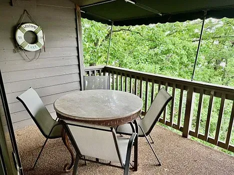 Patio with round table and four chairs. A life preserver hangs on the wall. Overlooking lush greenery.