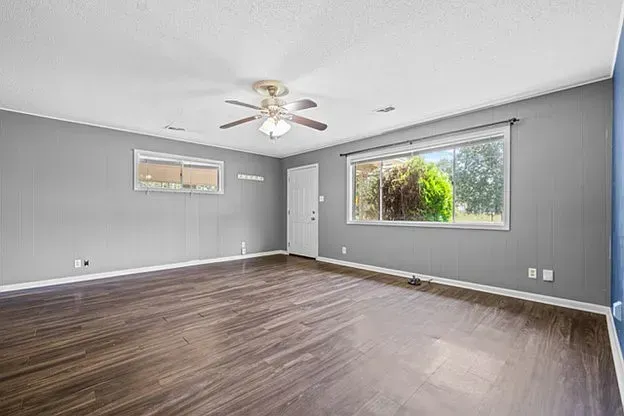 An empty living room with hardwood floors and a ceiling fan.