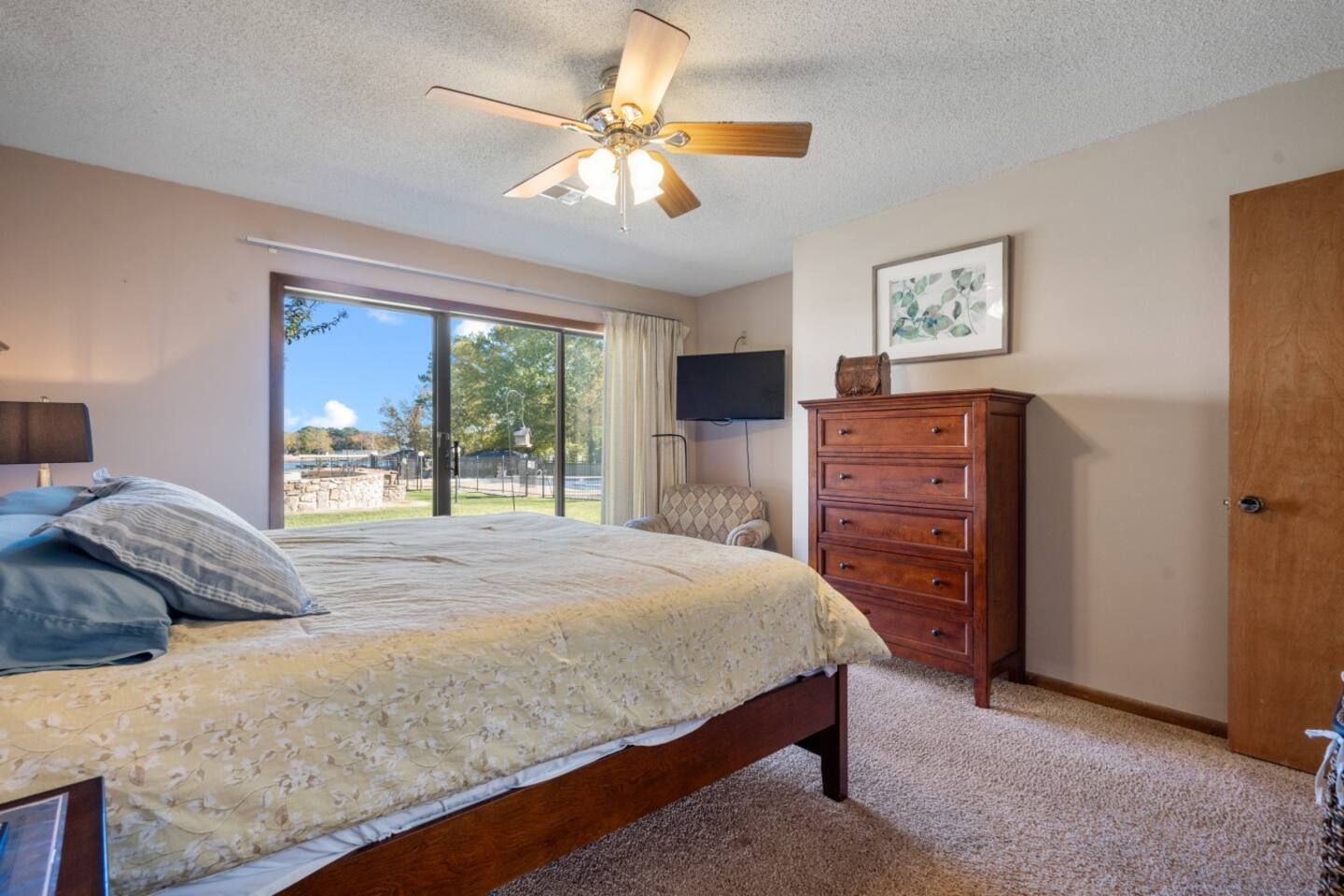 A bedroom with a bed , dresser , television and ceiling fan.