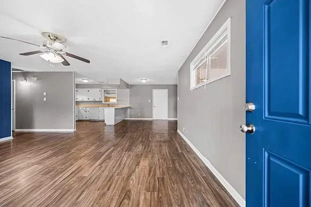 An empty living room with hardwood floors and a blue door.