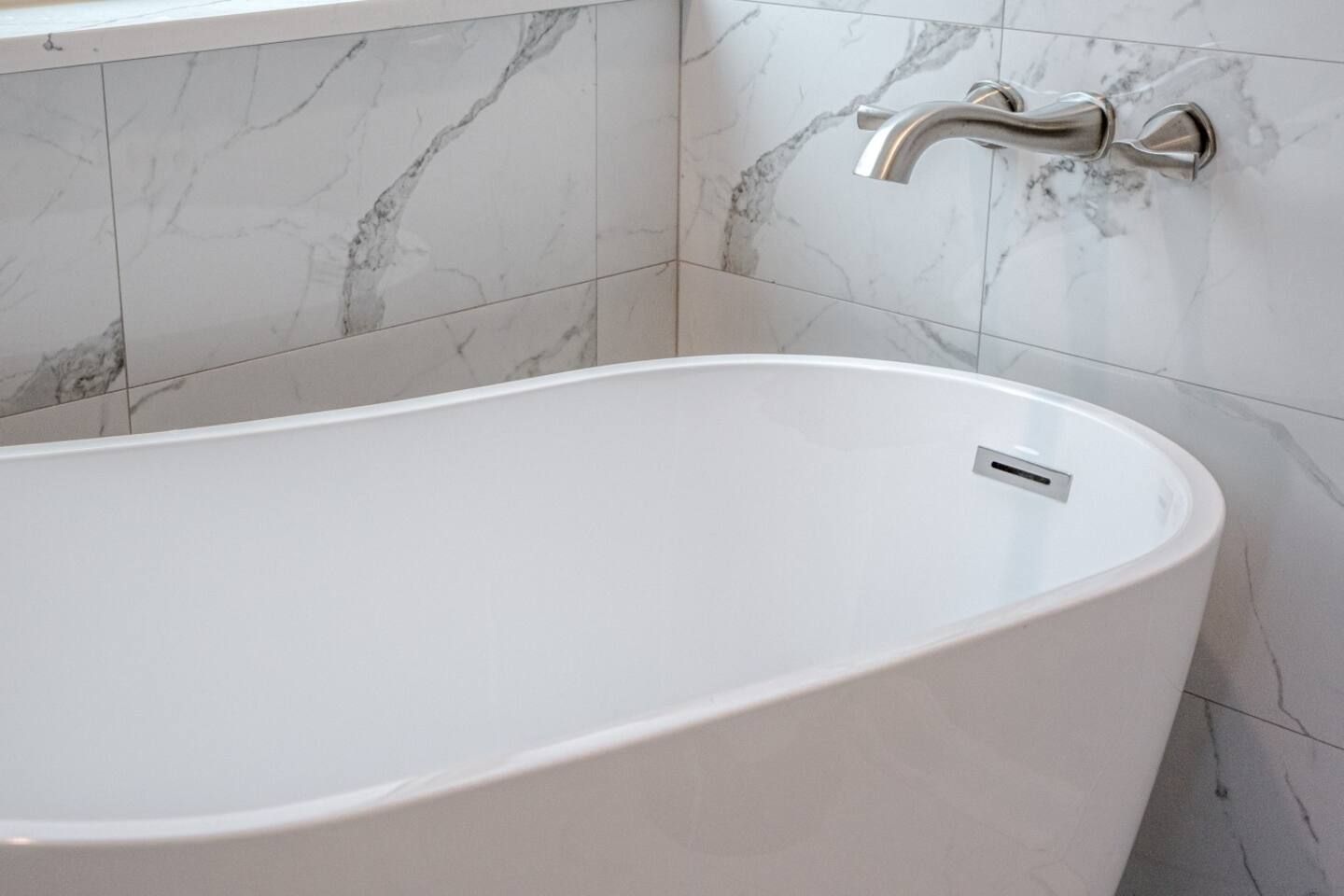 A white bathtub is sitting in a bathroom next to a marble wall.
