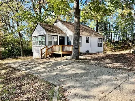 A small white house with a brown roof is sitting in the middle of a forest.