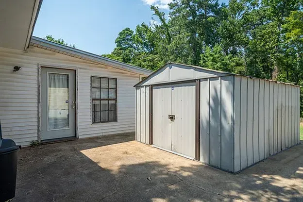 A white house with a metal shed in front of it.