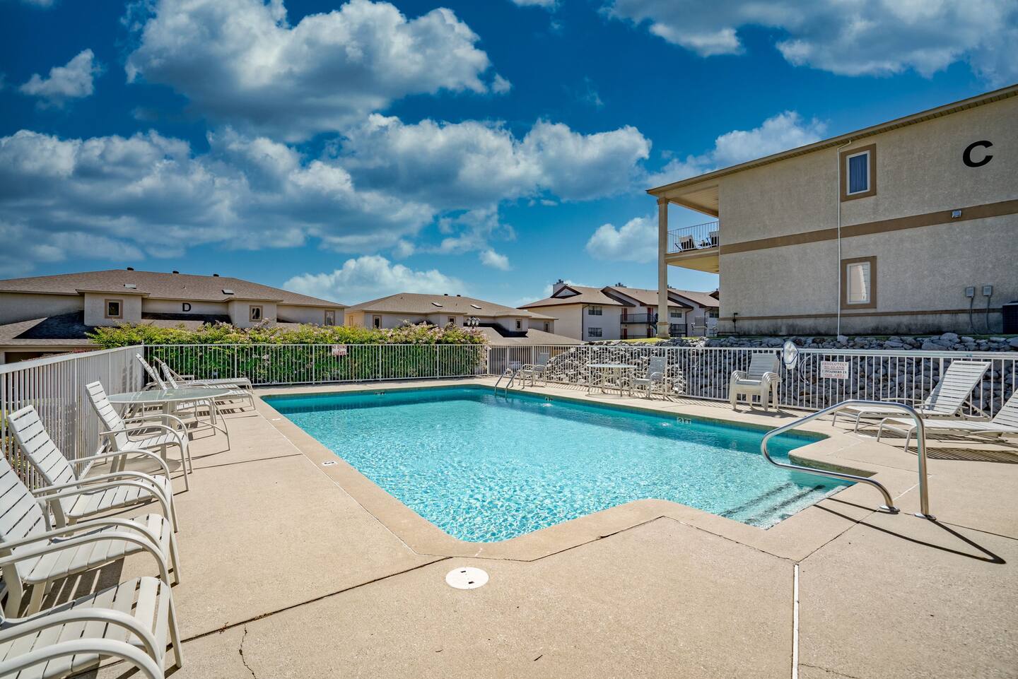 A large swimming pool is surrounded by chairs and a building.