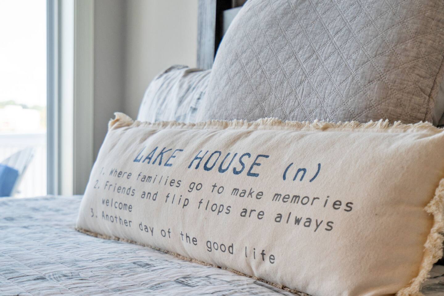 A pillow with the words `` lake house '' written on it is sitting on a bed.