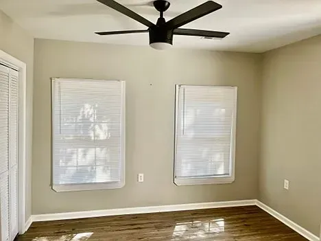 An empty room with two windows and a ceiling fan.