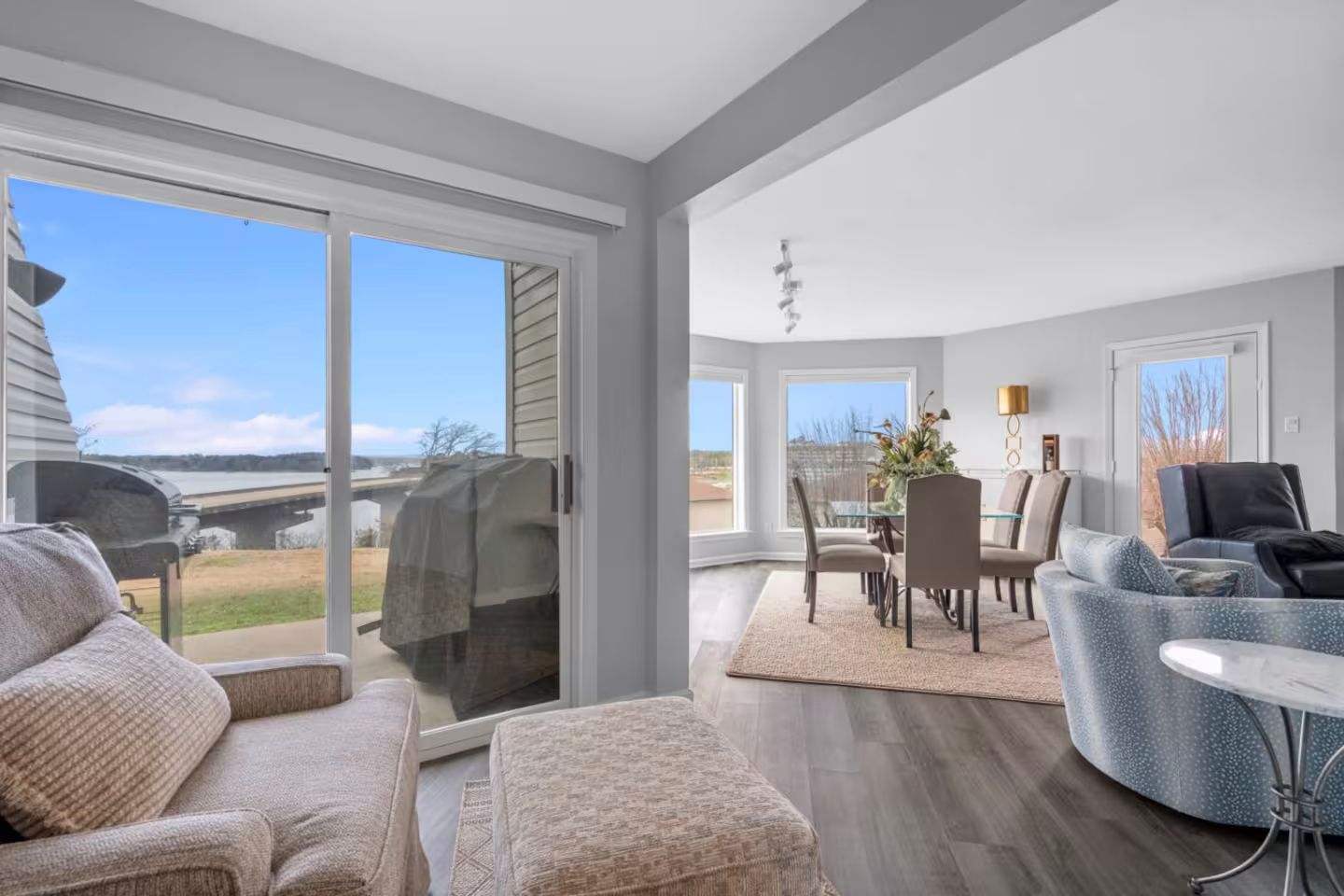 A living room with a couch , chair , ottoman and sliding glass doors leading to a dining room.