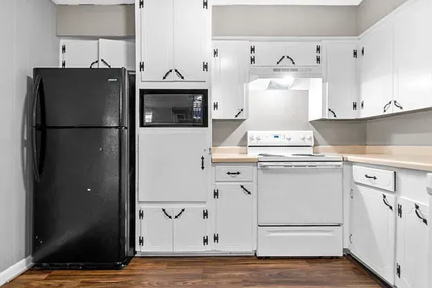 A kitchen with white cabinets , a black refrigerator , a stove , and a microwave.