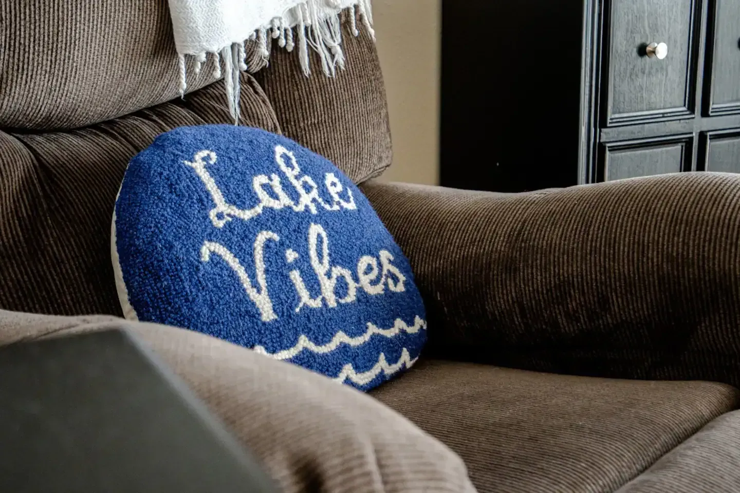 A chair with a blue pillow on it that says `` lake vibes ''.