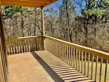 A porch with a wooden railing and trees in the background.