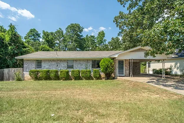 A house with a large lawn in front of it and trees in the background.