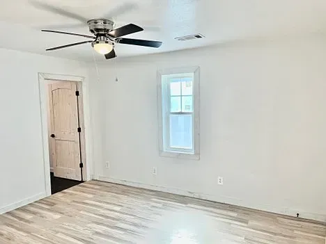 An empty room with a ceiling fan and a window.