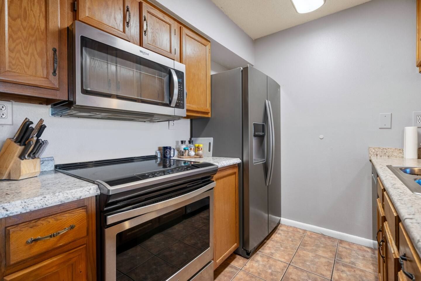 A kitchen with a stove , refrigerator , microwave and sink.