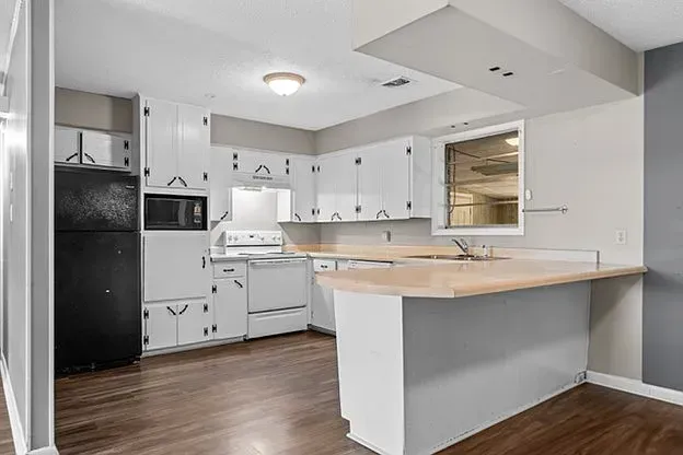 A kitchen with white cabinets , a black refrigerator , a microwave , and a window.