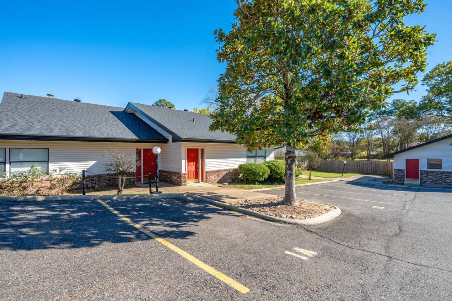 A white house with a red door and a parking lot in front of it.