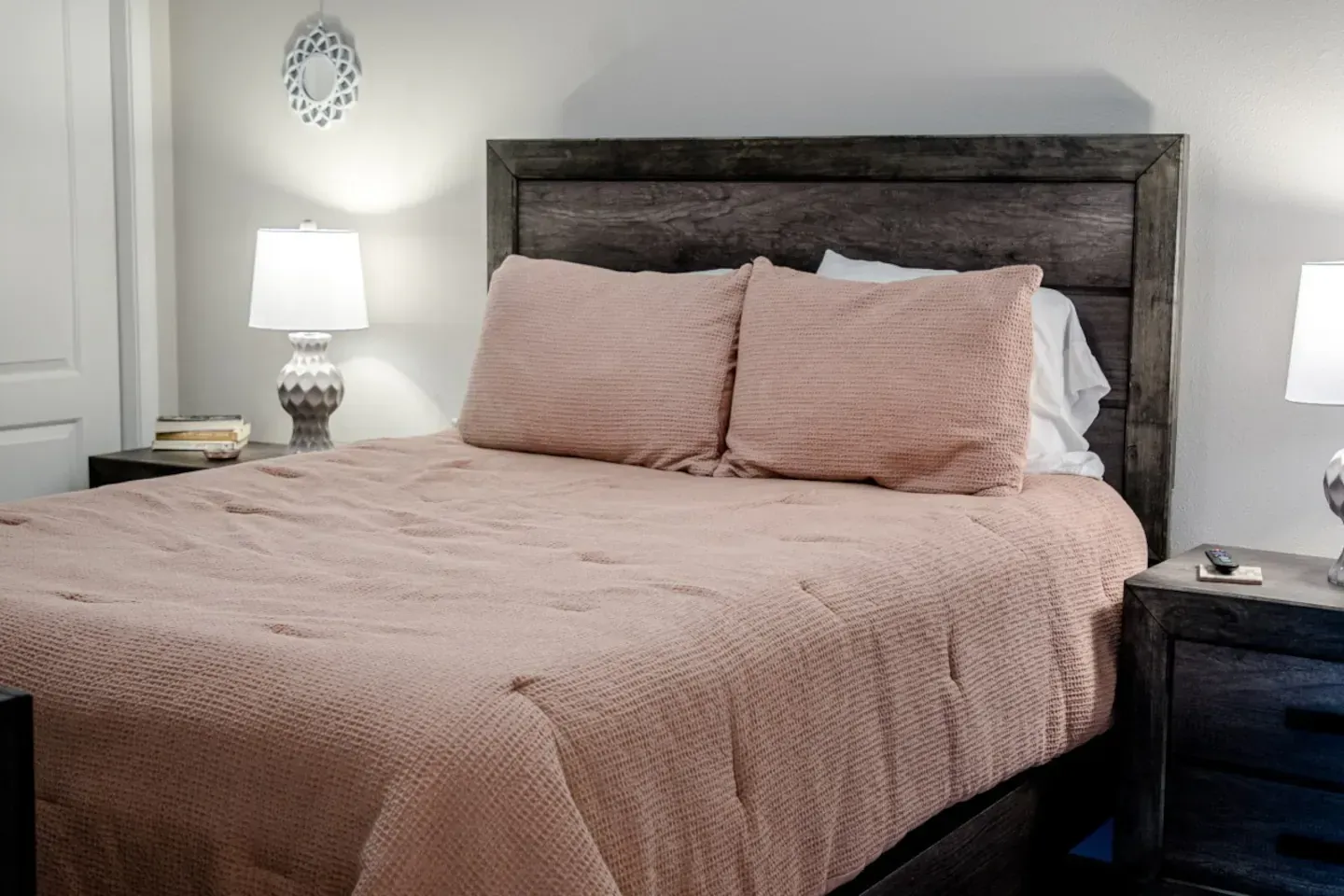 A bedroom with a bed , nightstand , lamp and wreath on the wall.