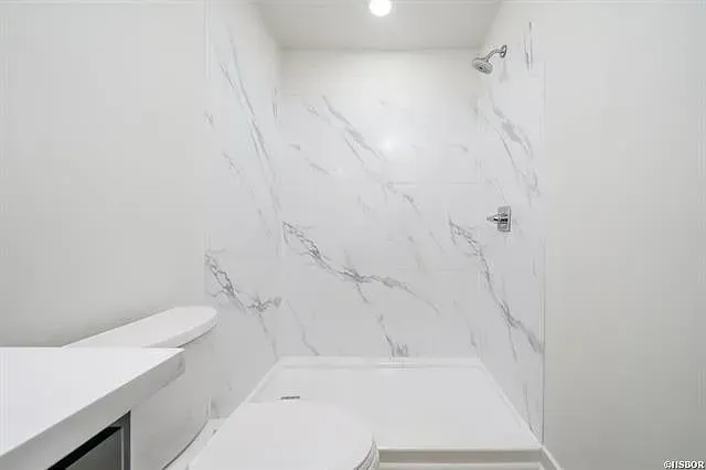 A bathroom with a toilet , shower and marble walls.
