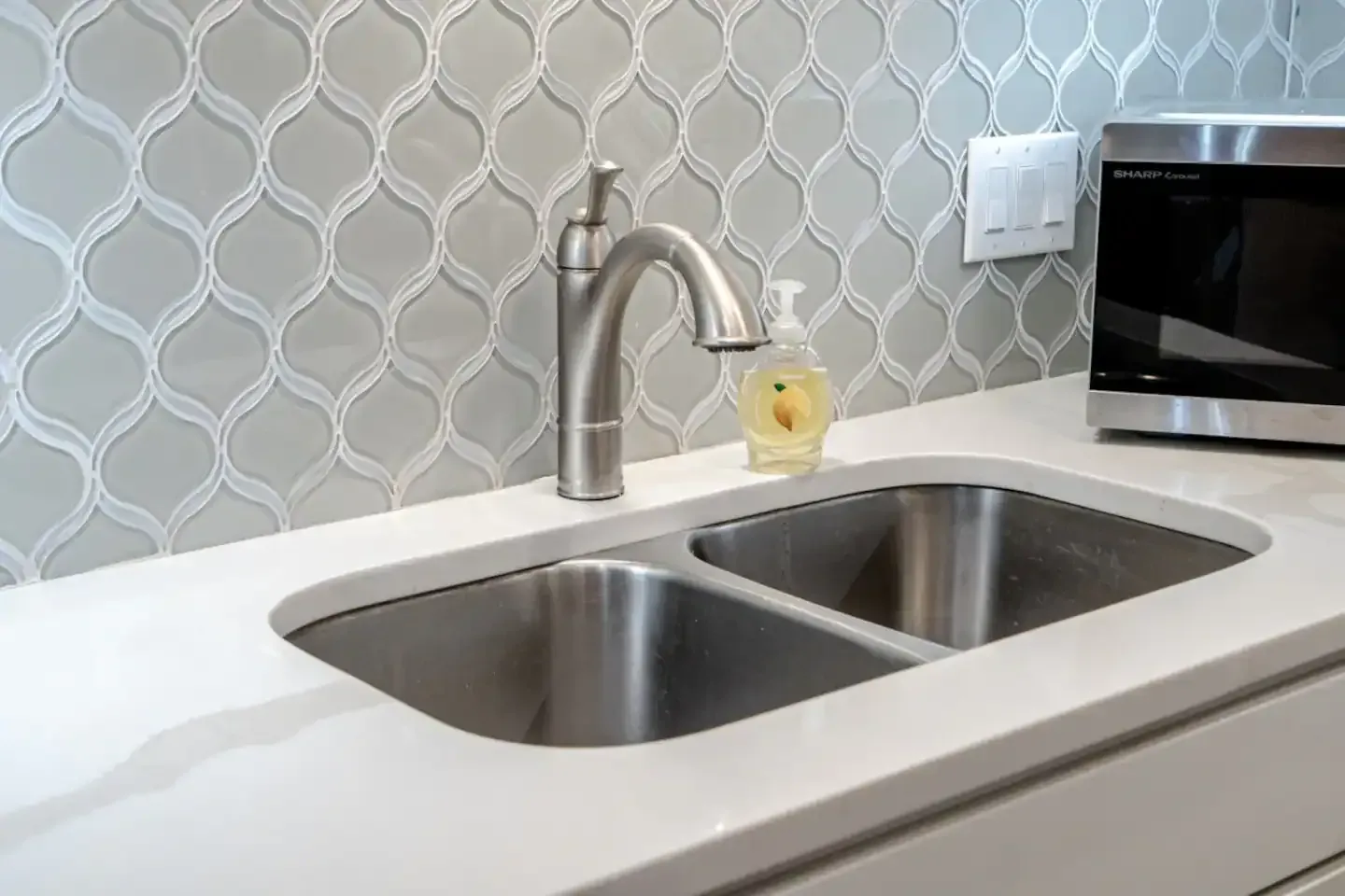 A kitchen sink with a soap dispenser and a microwave.