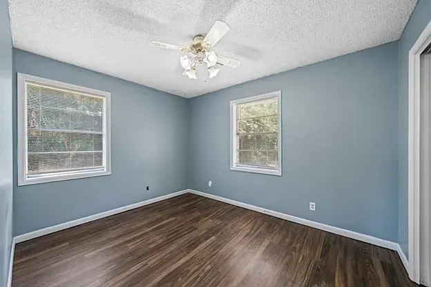 An empty bedroom with blue walls and hardwood floors and a ceiling fan.